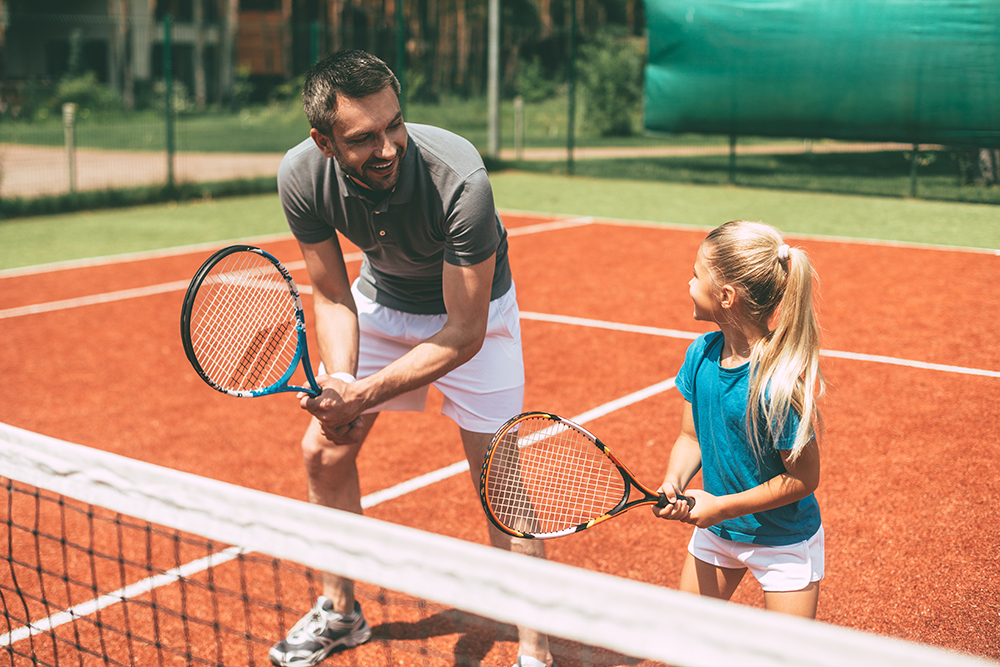Father and daughter practice tennis at a sports complex