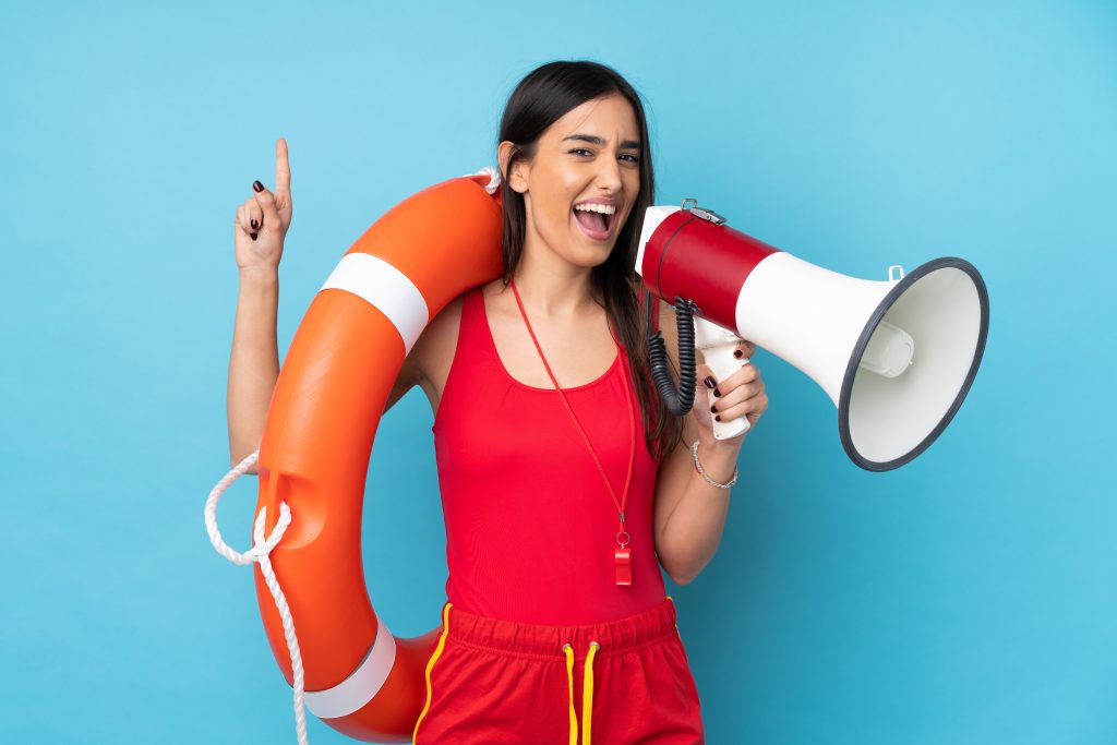 Lifeguard woman over isolated blue background with lifeguard equipment and shouting through a megaphone