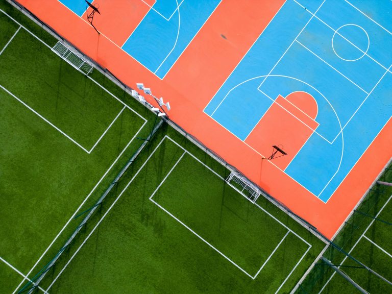 aerial view of a green football field and a colorful basketball court, providing a glimpse of two different sports facilities side by side.